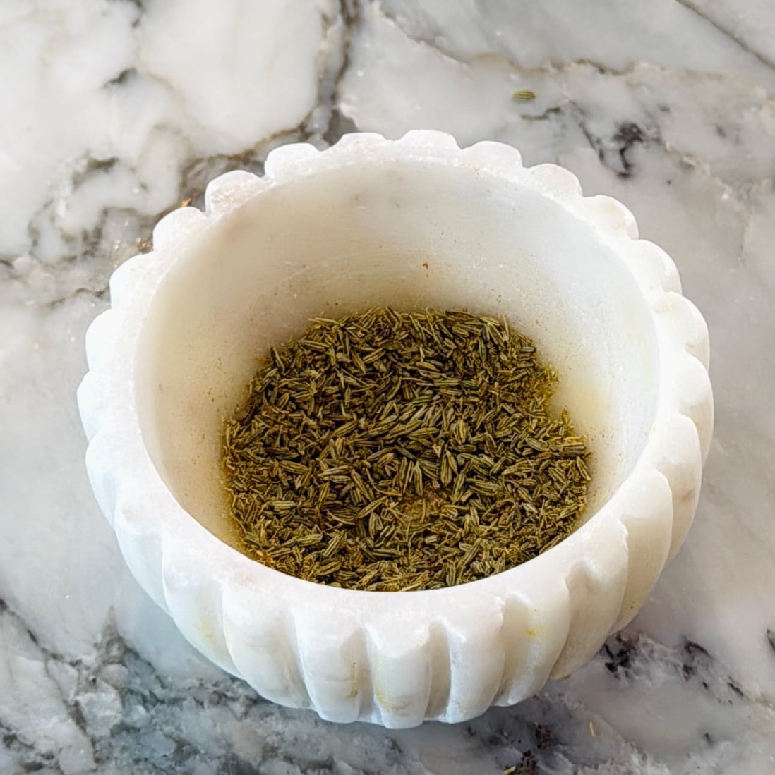 A small white marble bowl filled with dried green herbs.