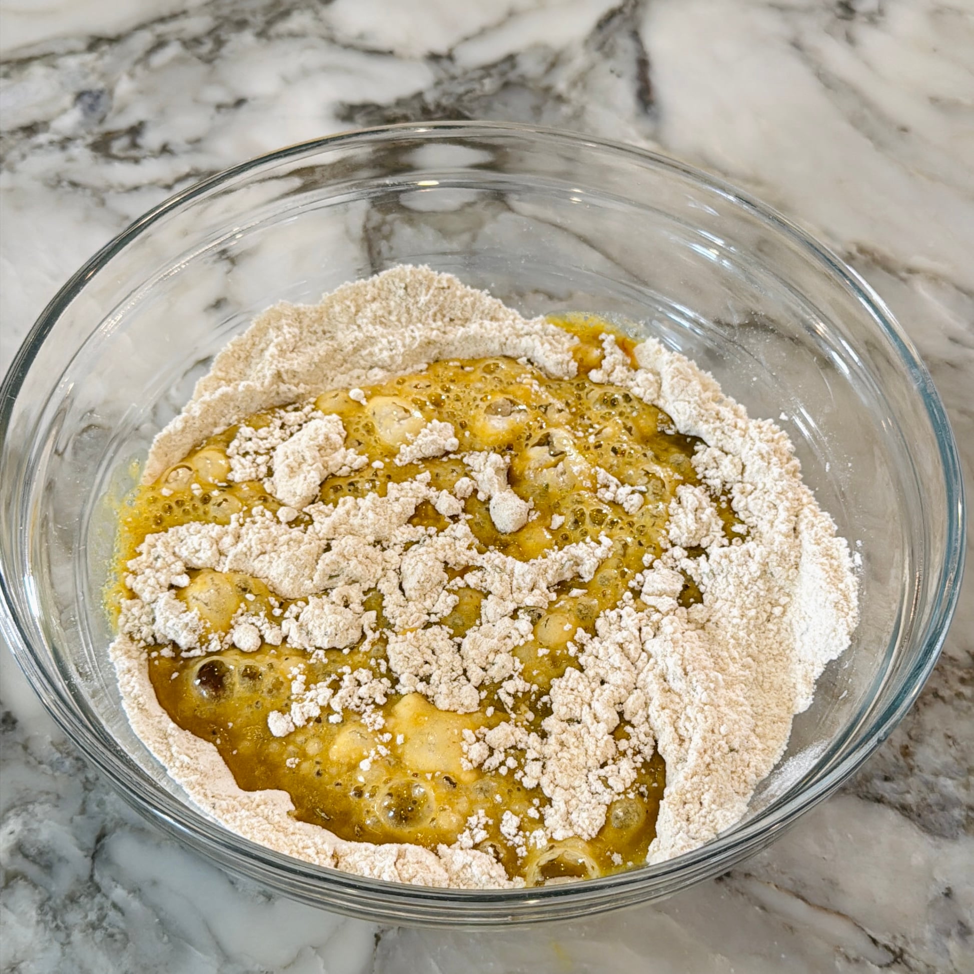 A glass bowl containing a mixture of flour and beaten eggs.