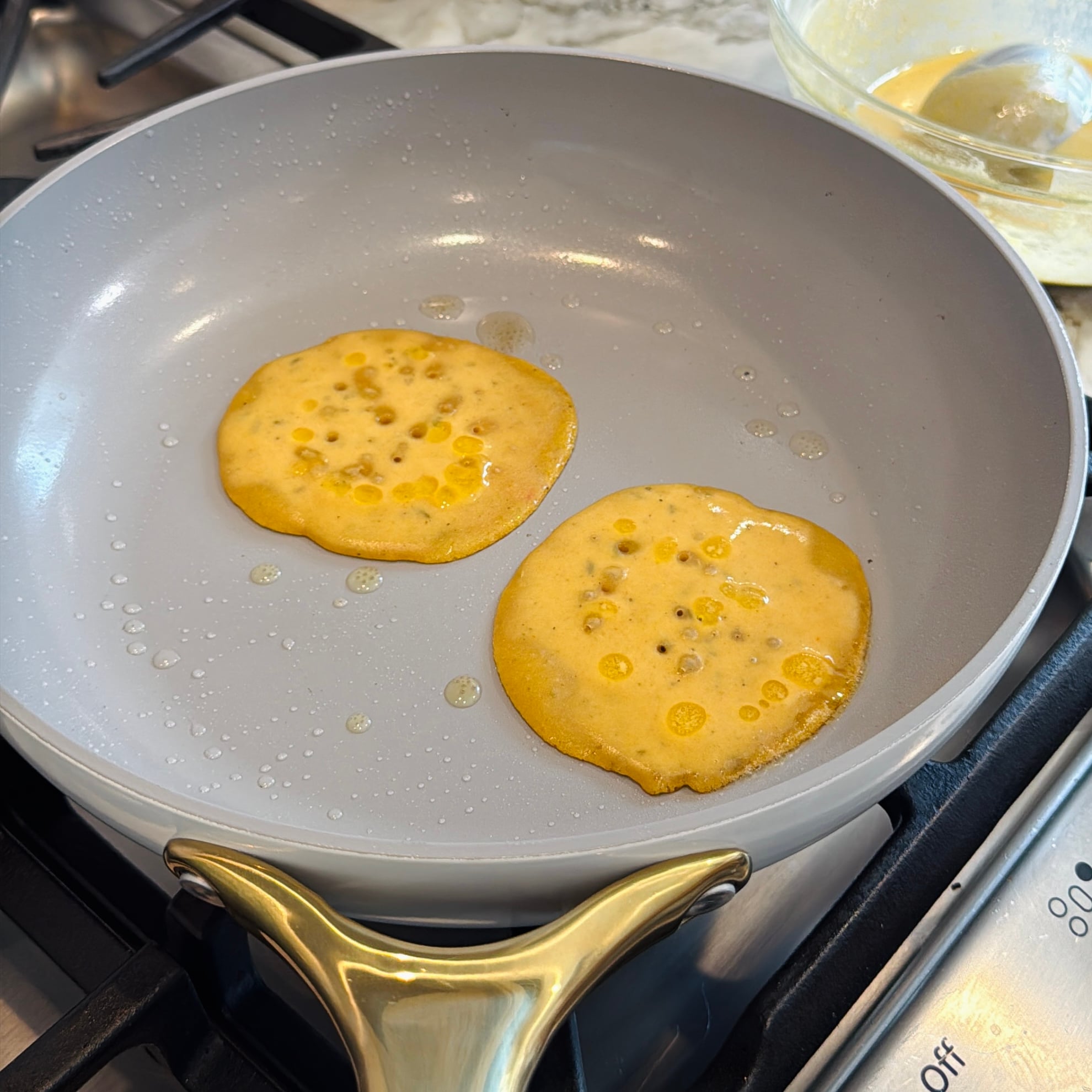 Two small pancakes cooking in a grey non-stick skillet.