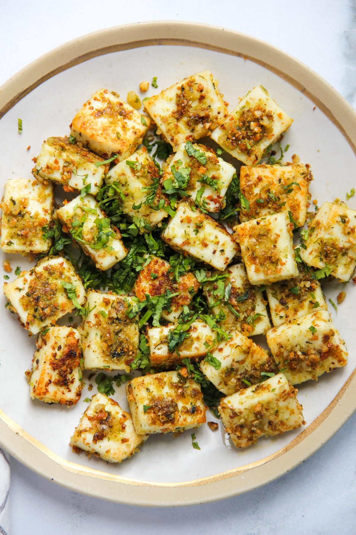 A plate of pan-fried paneer cubes garnished with chopped herbs and spices.