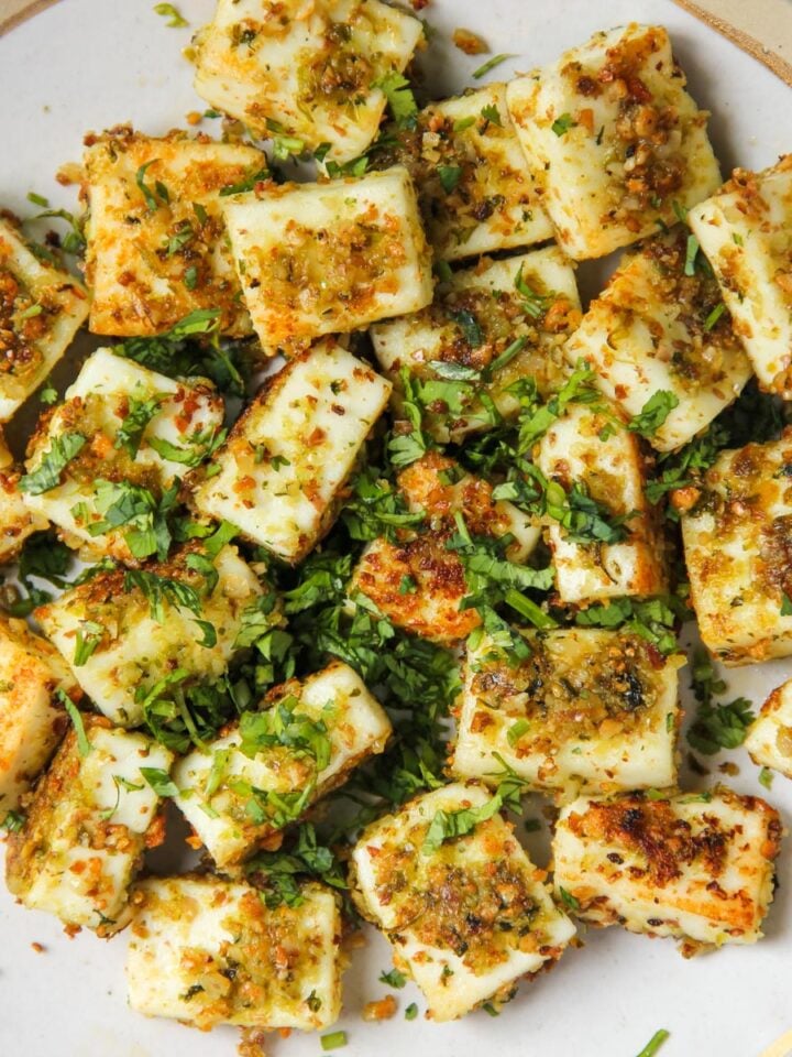 A plate of cubed, pan-seared paneer cheese garnished with chopped herbs and spices.