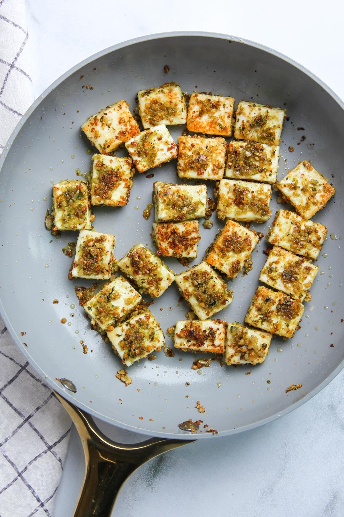 Cubes of seared cheese topped with herbs and spices in a grey frying pan.